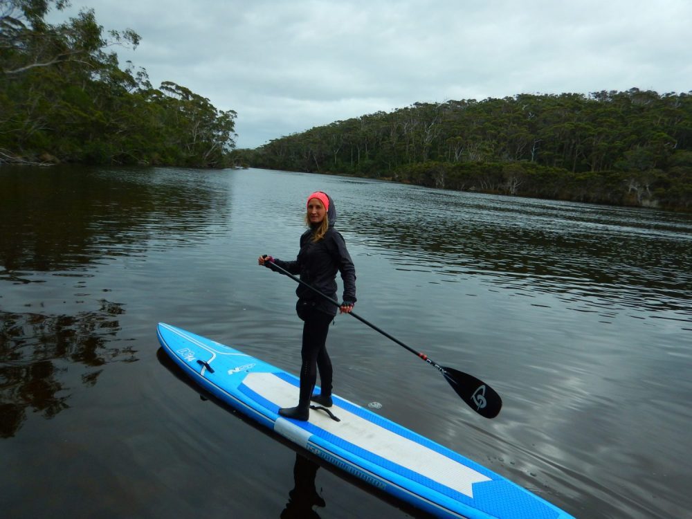 a woman standing on a paddle board in the swan river during winter