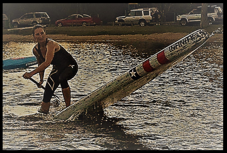 A grainy photo of Maree 2014 on a Sup Paddle Board, with the nose of the board in the air, out of the water.